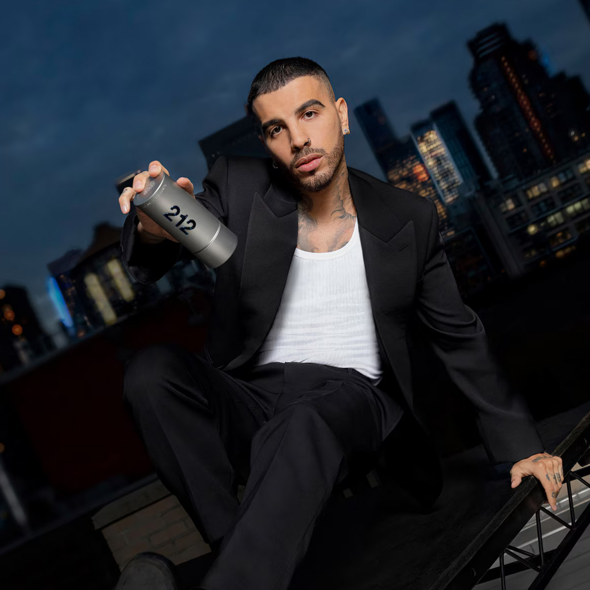 Hombre sosteniendo el perfume 212 Men Carolina Herrera Hombre en un entorno urbano nocturno Rauw Alejandro